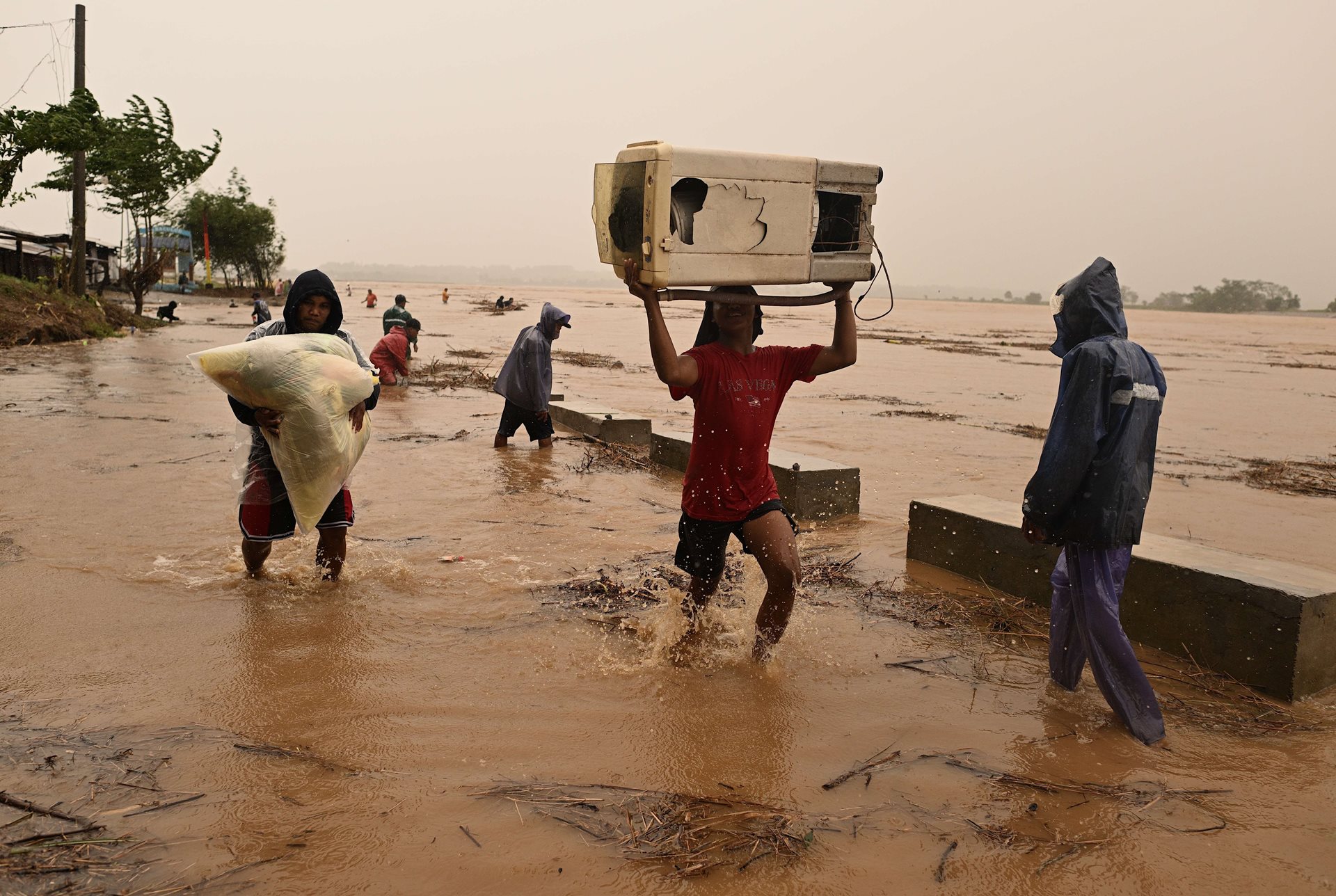 Residents carry their belongings as the river swells, in Ilagan City, Isabela, northern Philippines, following heavy rains from Typhoon Toraji. The typhoon knocked down trees, caused power outages, and blocked roads with debris, complicating relief efforts.&nbsp;